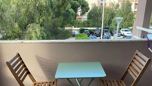 A balcony with two wooden folding chairs and a table, a view of parked cars and trees, and a building in the background.