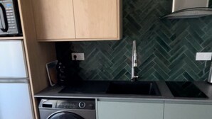 A compact kitchen with a washing machine, a microwave, and a sink with a herringbone-patterned backsplash.