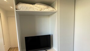 A walk-in closet with a television on a shelf, drawers below, and a bed at the top.