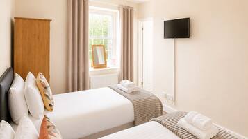 A hotel room with two beds, a wooden wardrobe, a window with curtains, a flat-screen TV, and a ceiling light.