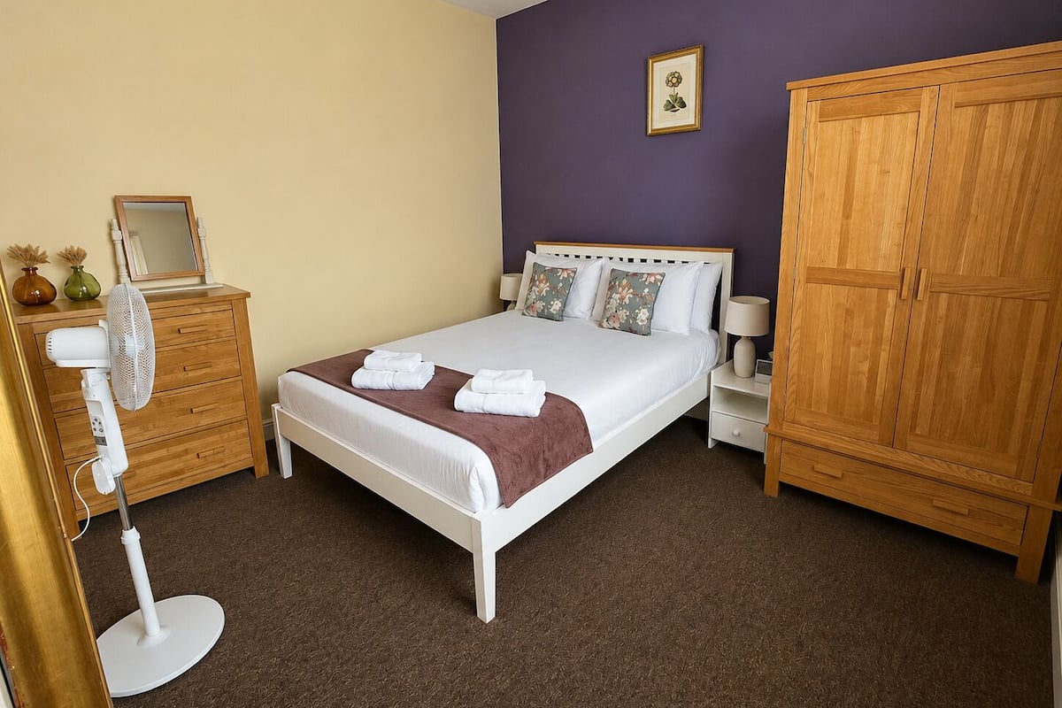 A bedroom with a bed, bedside table, wardrobe, and a mirror on a dresser.