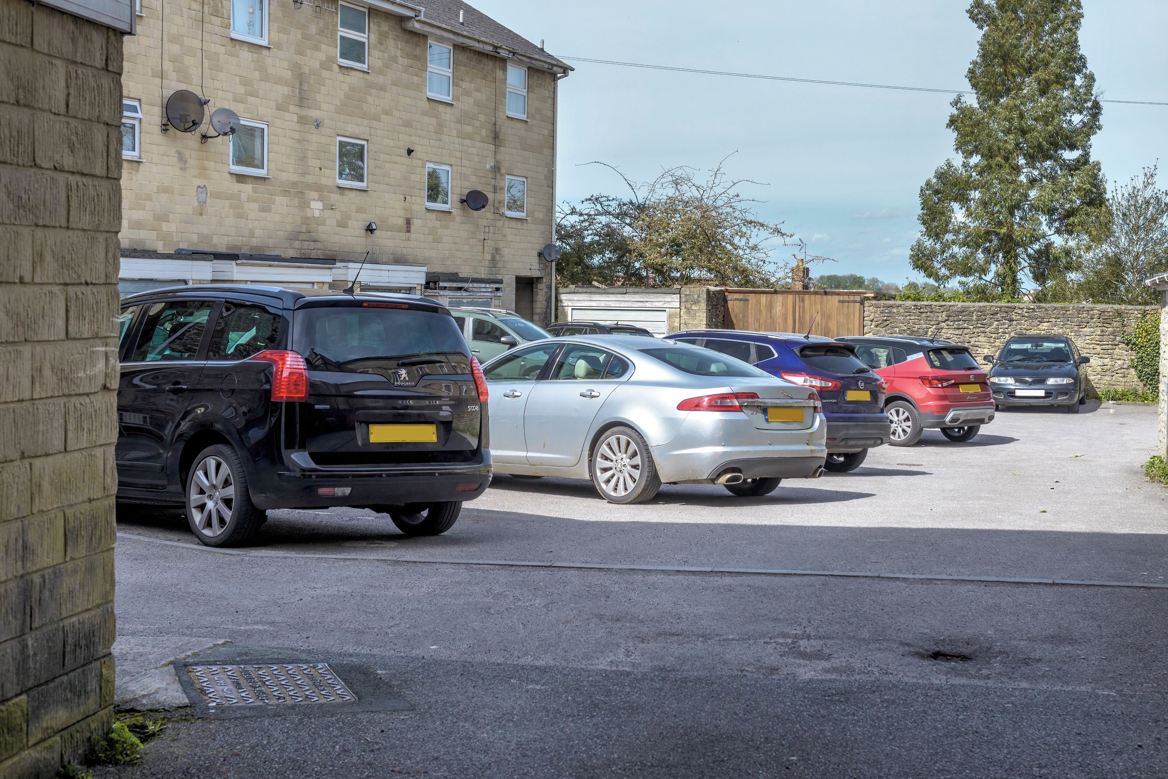 A parking lot with several cars parked in front of a building with satellite dishes and a garage.
