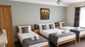 A hotel room with three beds, a wooden wardrobe, a painting on the wall, and a window with curtains. - The Cornerhouse (Frome)