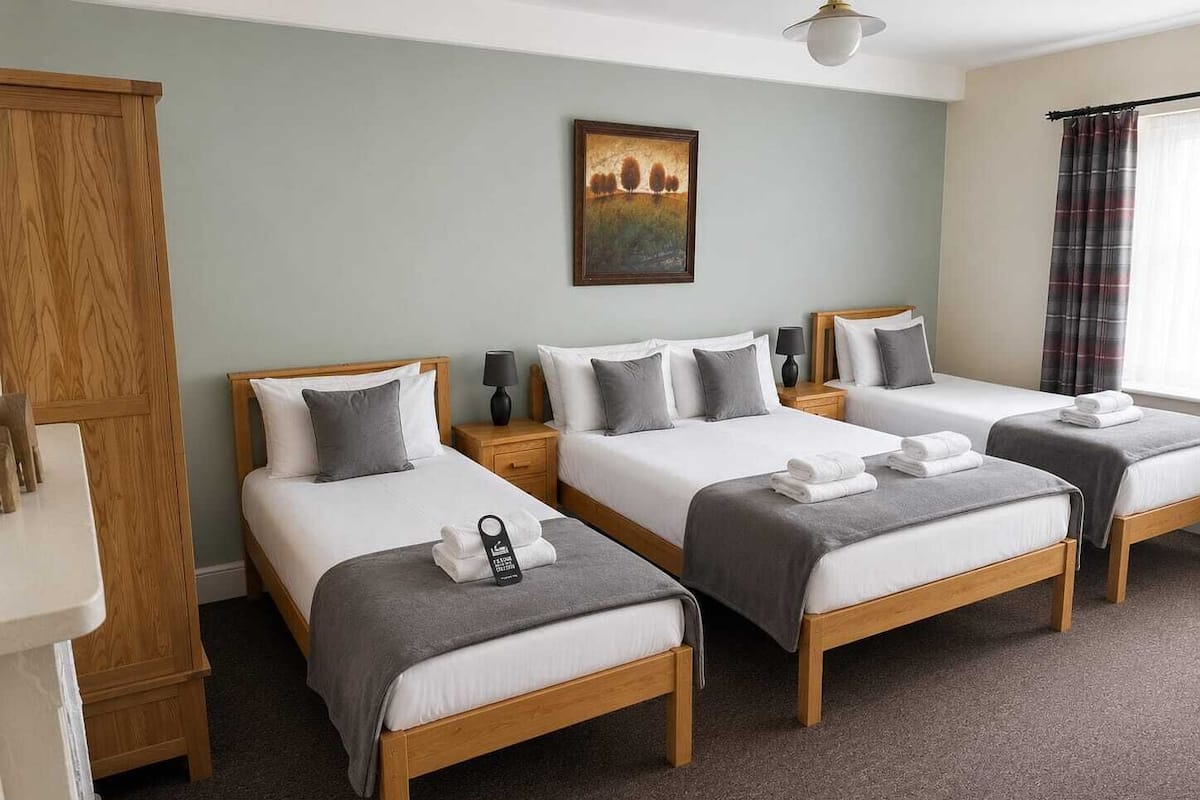 A hotel room with three beds, a wooden wardrobe, a painting on the wall, and a window with curtains.