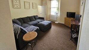 A living room with a sofa, a small table, a TV, and a radiator. - The Cornerhouse (Frome)