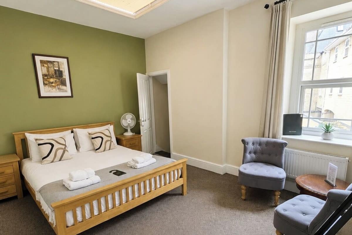 A bedroom with a bed, bedside table, chair, and a window with a view of buildings.