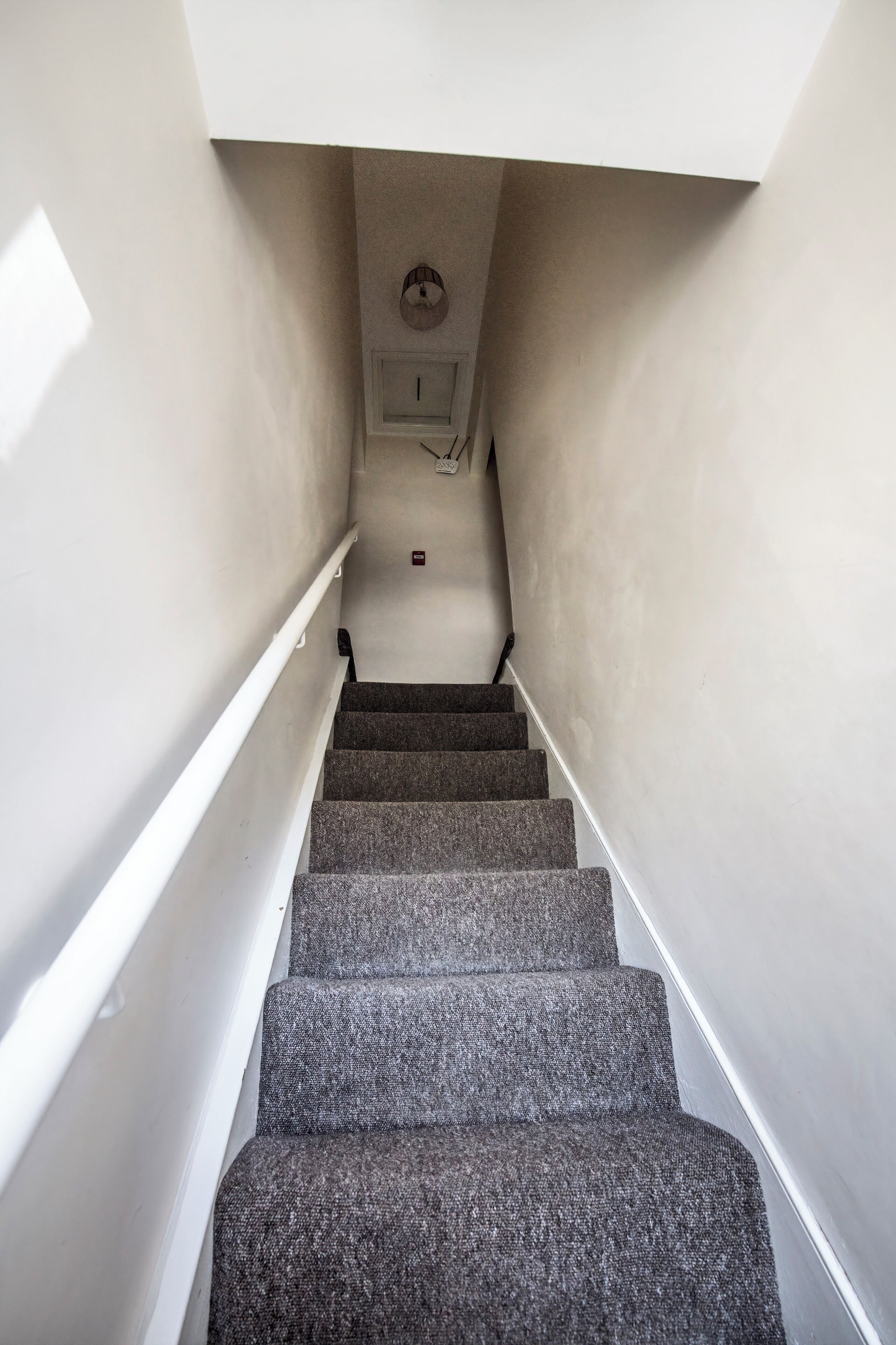 Una escalera con peldaños alfombrados que conduce a una plataforma con un interruptor de luz y un detector de humo.