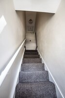 Una escalera con peldaños alfombrados que conduce a una plataforma con un interruptor de luz y un detector de humo.