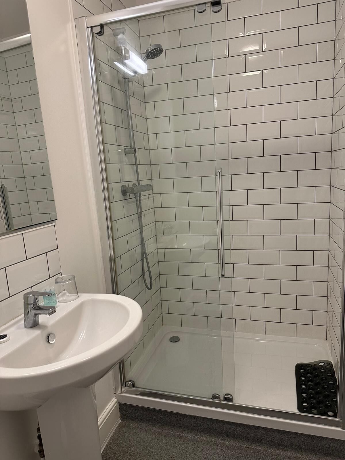Ett badrum med en dusch som är avskärmad med glasväggar, ett handfat och en spegel.