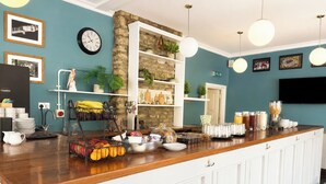 A breakfast bar with a stone accent wall, white cabinetry, and various breakfast items. - The Cornerhouse (Frome)