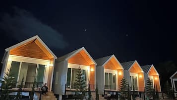 A row of modern, single-story cabins with large windows and a wooden facade, set against a night sky.