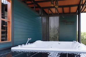 Een wellnessruimte met een ruime witte jacuzzi, houten planken en een wand in blauwgroen.