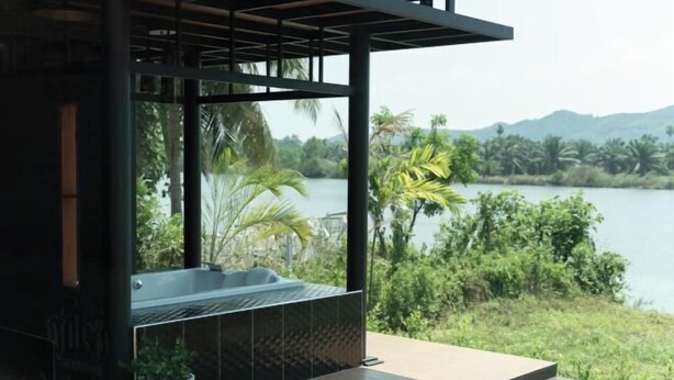 A modern outdoor spa area with a hot tub, surrounded by lush greenery and a view of a lake. - Huather Villa & Cafe (Lang Suan)