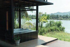 A modern outdoor spa area with a hot tub, surrounded by lush greenery and a view of a lake. - Huather Villa & Cafe (Lang Suan)