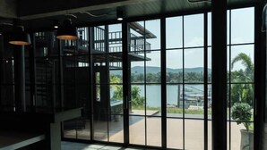 A room with large windows offering a view of a body of water and a deck area. - Huather Villa & Cafe (Lang Suan)