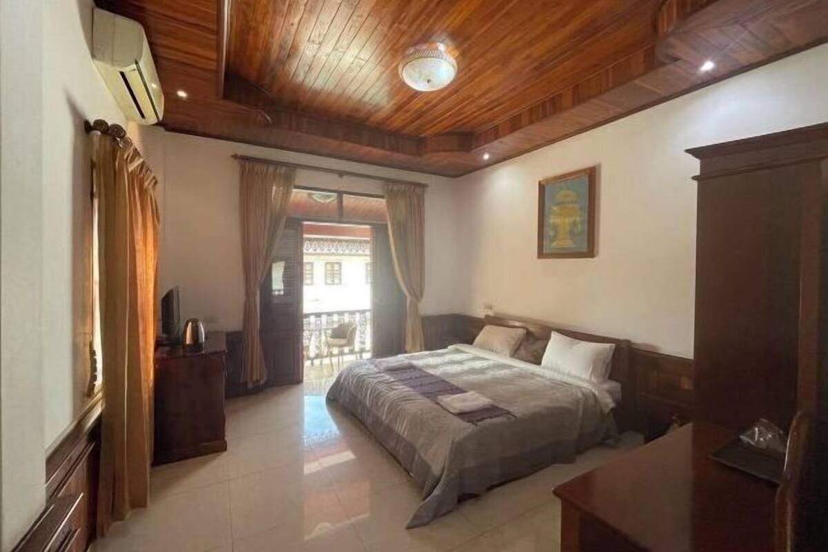 A bedroom with a wooden ceiling, a bed with a grey and white duvet, a wooden nightstand, and a painting on the wall.
