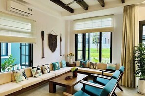 A spacious living room with a long sofa, a coffee table, and a view of the outdoors. - 3 bedroom seafront Cherry Villa - Novaworld Phan Thiet (Phan Thiet)