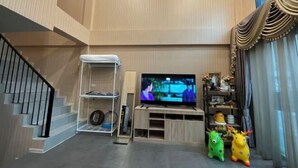 A living room with a flat-screen TV on a wooden stand, a staircase, and a shelf with decorative items. - My Own House SURAT THANI (Surat Thani)