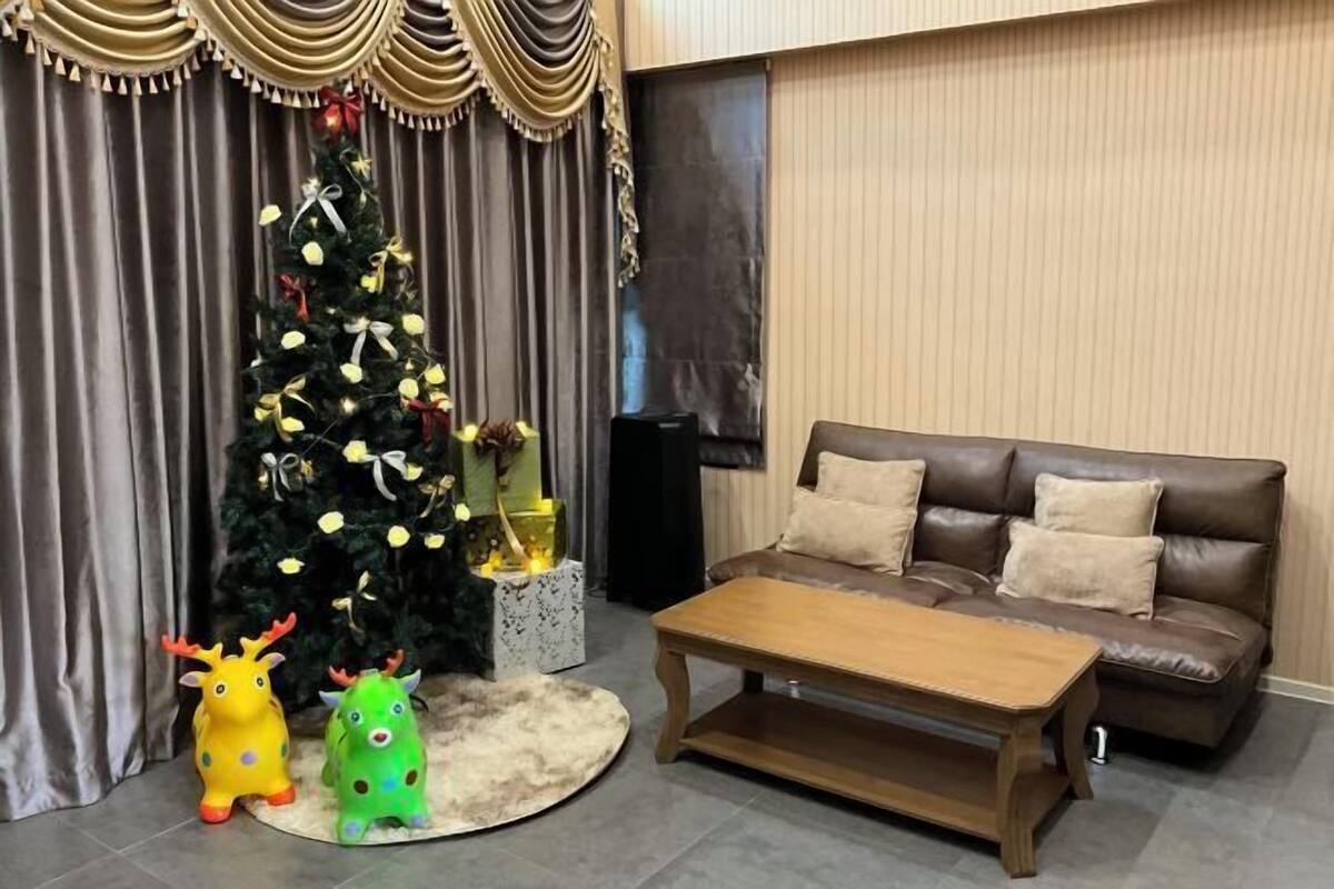 A living room with a brown leather sofa, a wooden coffee table, a Christmas tree, and two toy reindeer.