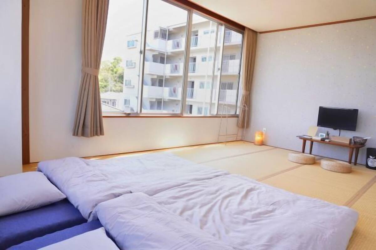 Une chambre d’hôtel avec une grande fenêtre, un lit, une télévision et des tatamis au sol.