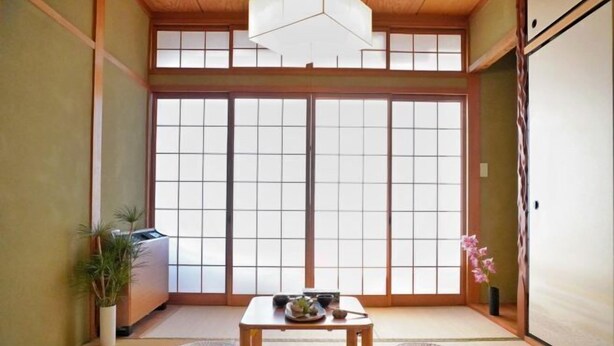 Ein traditioneller japanischer Raum mit Tatami-Bodenbelag, einem niedrigen Tisch mit Schüssel und Stäbchen sowie einer Schiebetür mit Gittermuster.