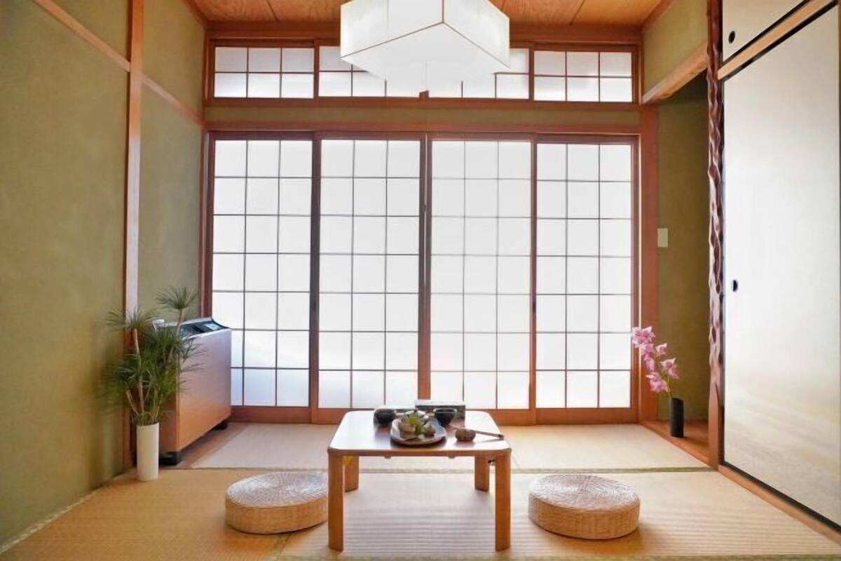 Une pièce de style japonais traditionnel, avec un sol recouvert de tatamis, une petite table sur laquelle se trouvent un bol et des baguettes, et une porte coulissante ornée d’un motif à carreaux.