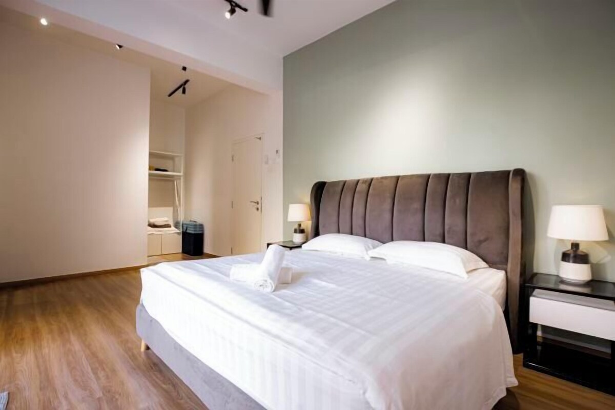 A neatly made bed with a pillow and a folded towel, a bedside table with a lamp, and a wardrobe in the background.