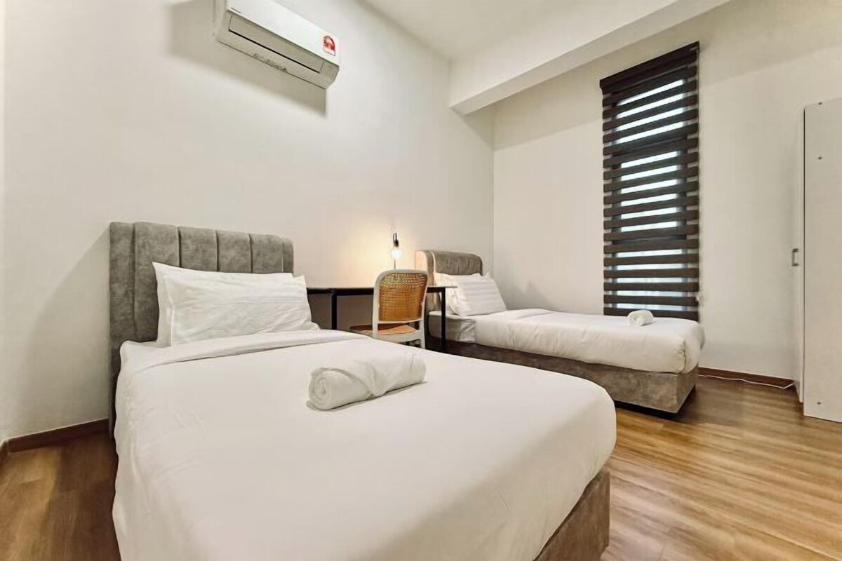 A hotel room with two beds, a window with blinds, a wall-mounted air conditioner, and a wooden floor.