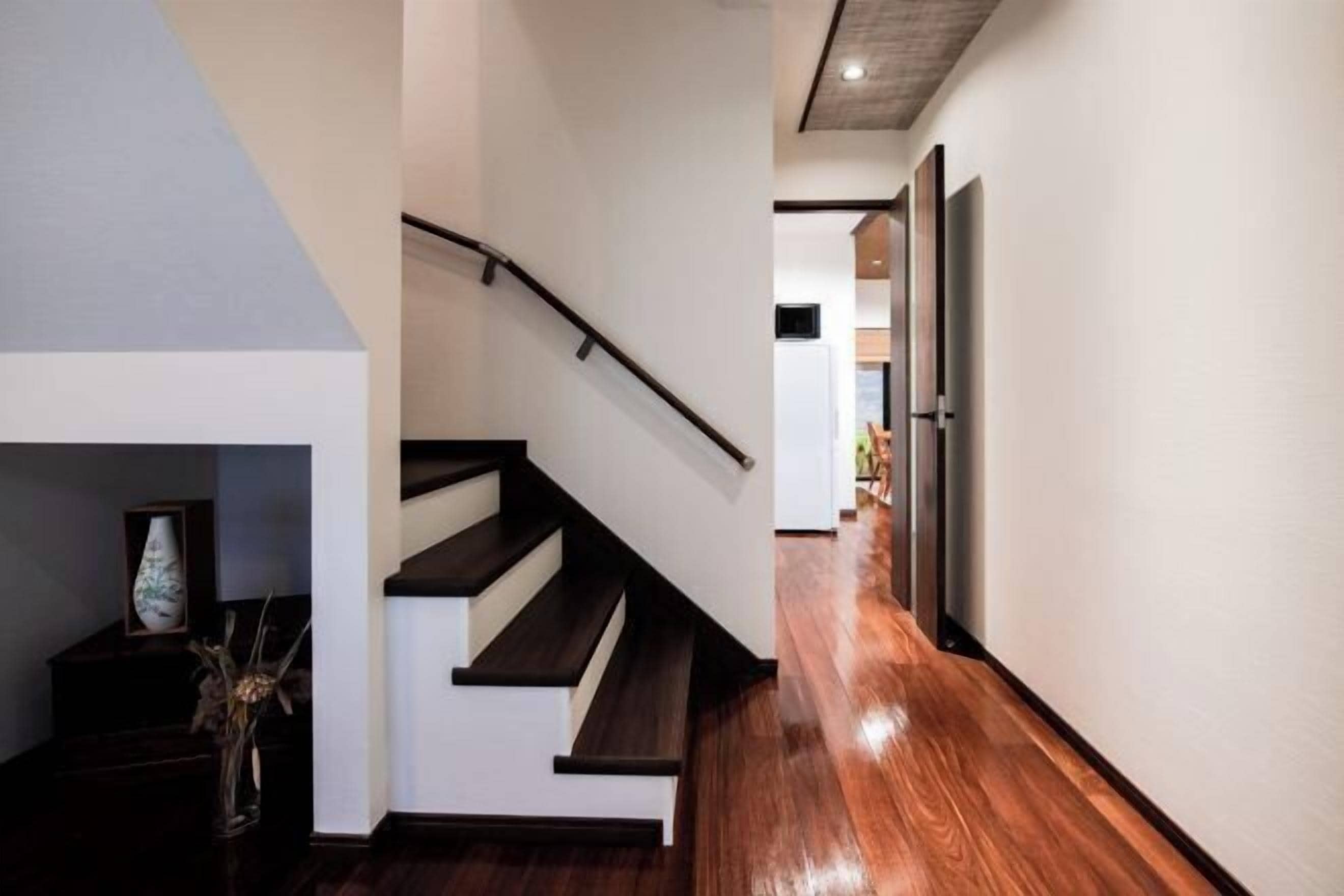 A modern staircase with wooden steps and a metal handrail, leading to a hallway with a wooden floor.