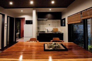 A modern kitchen with a central island, a dining area with a wooden table, and a view of greenery through a large window. - Kyoto Amazing The Wizarad of Oz (Kyoto)