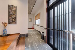 A hallway with a tiled floor, a blue vase with dried flowers, a framed artwork, and a black-framed window with vertical blinds. - Kyoto Amazing The Wizarad of Oz (Kyoto)
