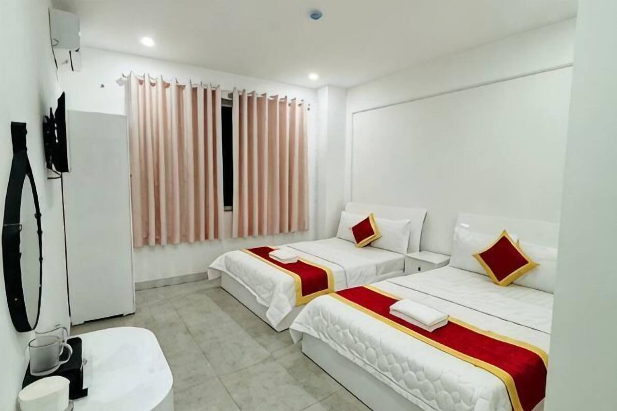 Une chambre d’hôtel avec deux lits, une télévision, une fenêtre avec des rideaux et un lavabo.