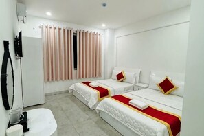 Ein Hotelzimmer mit zwei Betten, einem Fernseher, einem Fenster mit Vorhängen und einem Waschbecken.