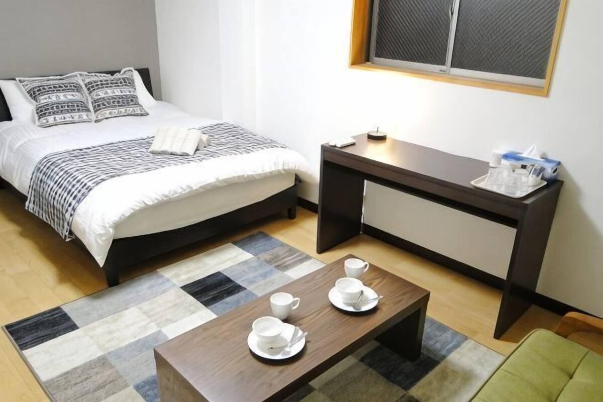 A neatly arranged bedroom with a bed, bedside table, and a coffee table with cups and saucers.