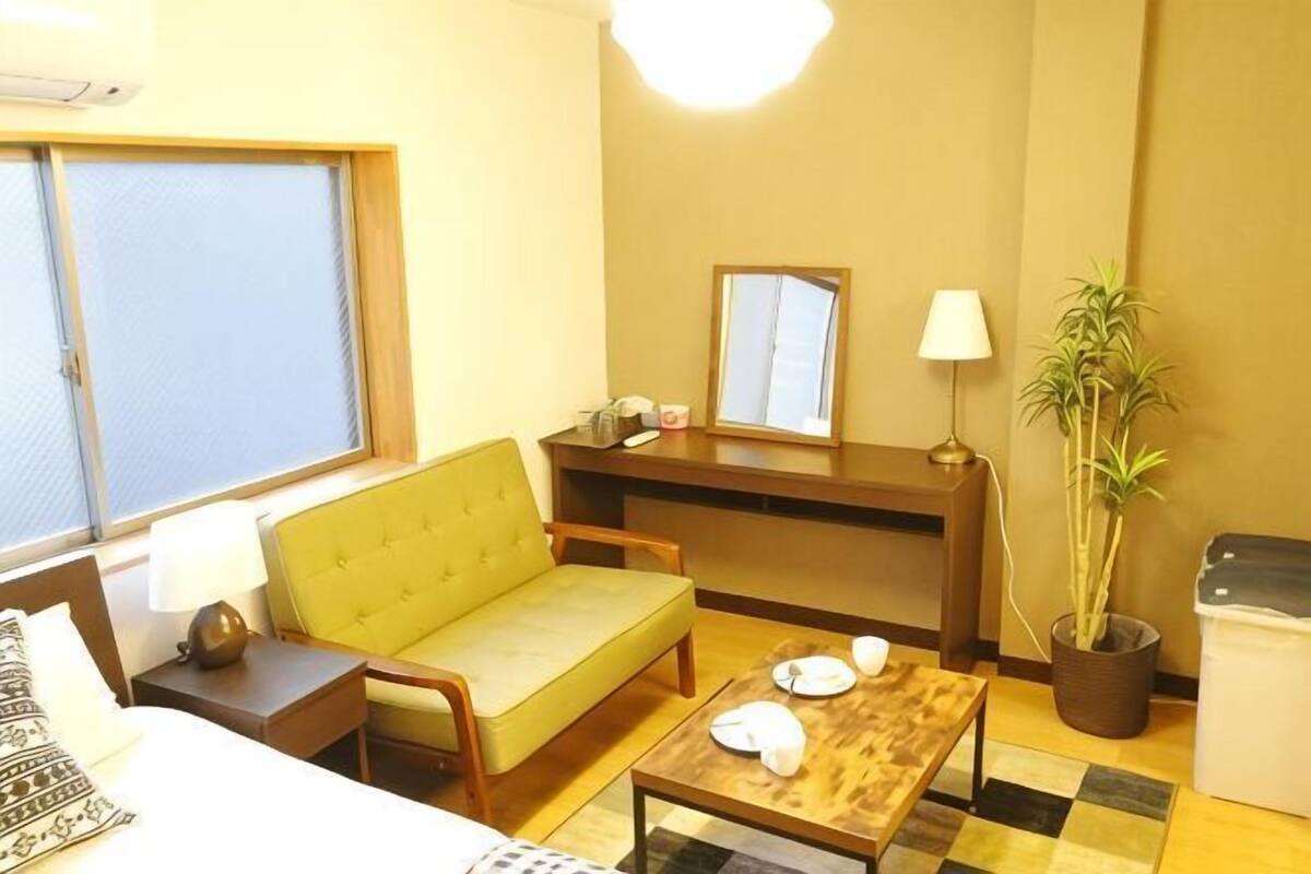 A hotel room with a bed, a sofa, a small table, a mirror, a lamp, and a potted plant.