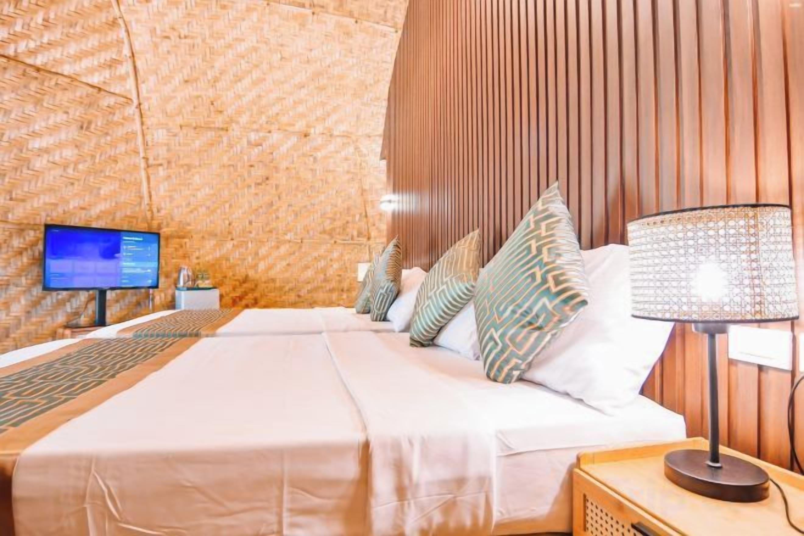 A hotel room with a large bed, a bedside table with a lamp, a TV on the wall, and a wooden panel wall.
