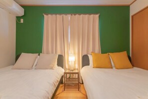 A room with two beds, a nightstand, a lamp, and a window with curtains. - Travel Time・Hanazonochō｜Direct train access to Shinsekai, Namba, and Dotonbori in 5 minutes (Osaka)