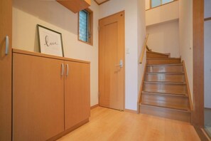 A wooden staircase leading to a landing with a door, a framed picture on the wall, and a wooden floor. - Travel Time・Hanazonochō|Direct train access to Shinsekai, Namba, and Dotonbori in 5 minutes (Osaka)