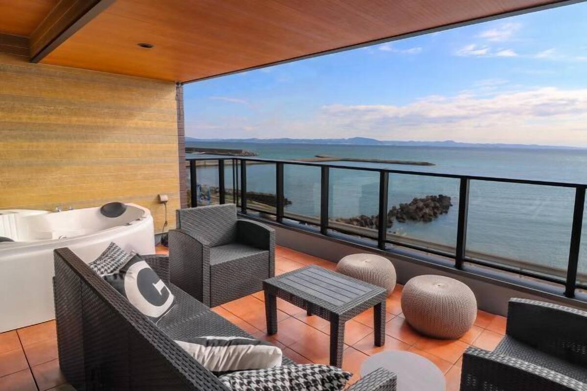 Un balcón con mobiliario de mimbre, un jacuzzi y vista al mar.