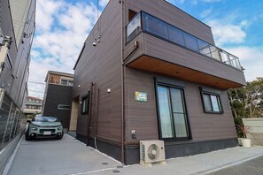En modern byggnad i två våningar med en balkong, stora fönster och en synlig luftkonditioneringsenhet.