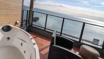 A balcony with a hot tub, wicker furniture, and a view of the ocean.