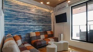 A modern living room with a sectional sofa, ottomans, a flat-screen TV, and a large window. - Le Grand Bleu Resort Nagasawa (Yokosuka)