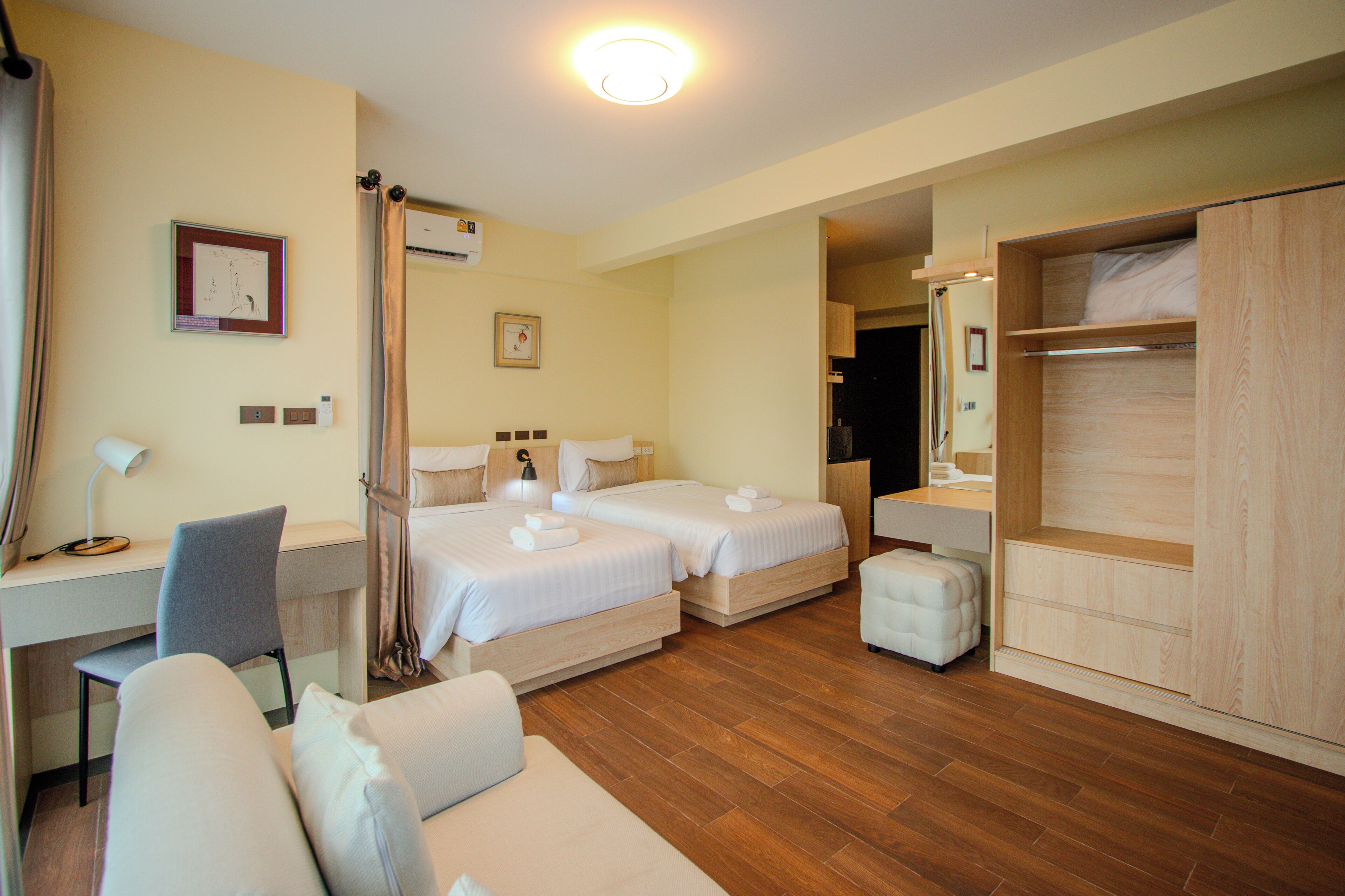 A hotel room with two beds, a desk, a chair, a sofa, and a wardrobe.