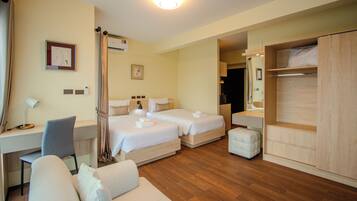 A hotel room with two beds, a desk, a chair, a sofa, and a wardrobe.