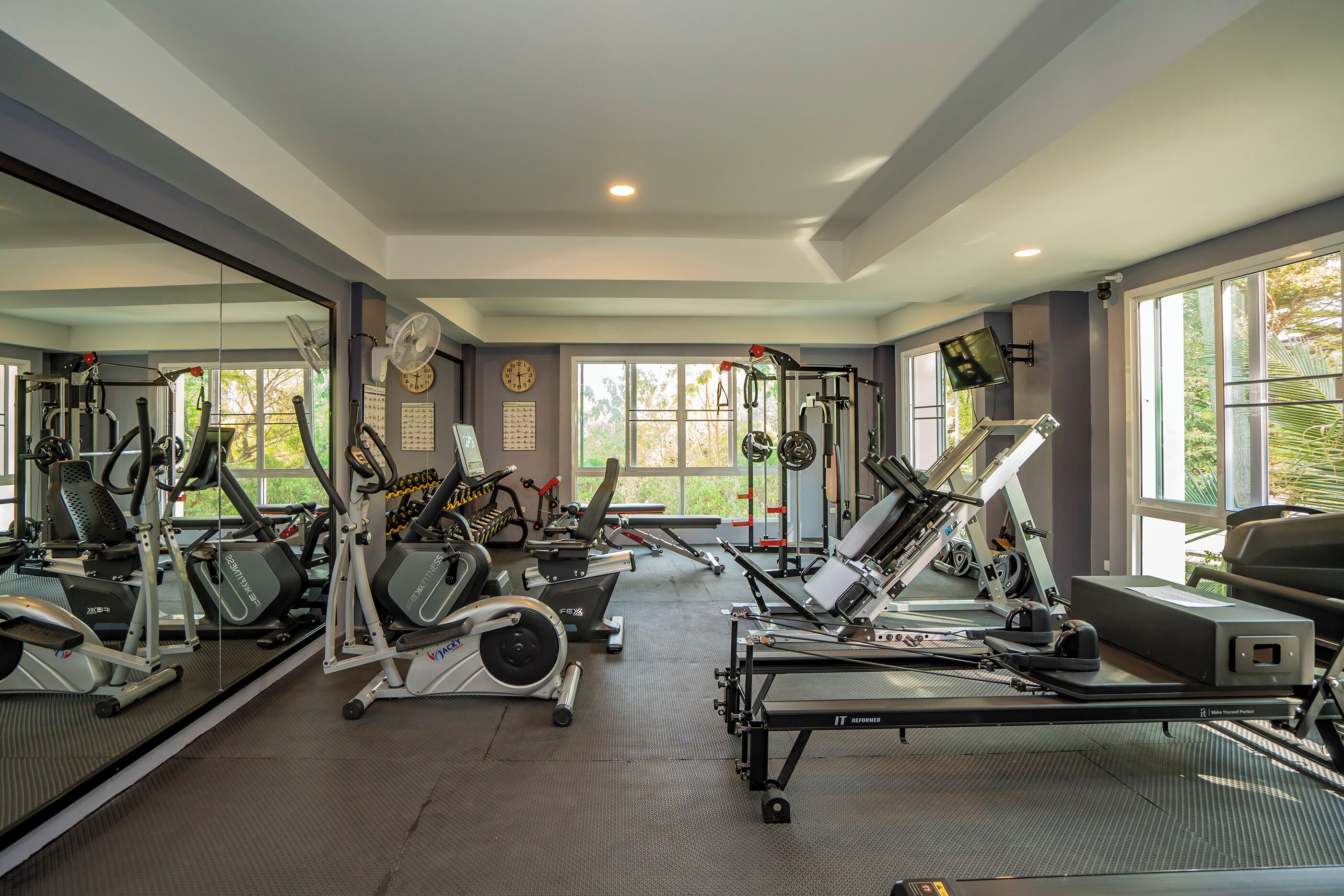 A gym with various exercise equipment, large windows, and a mirror wall.