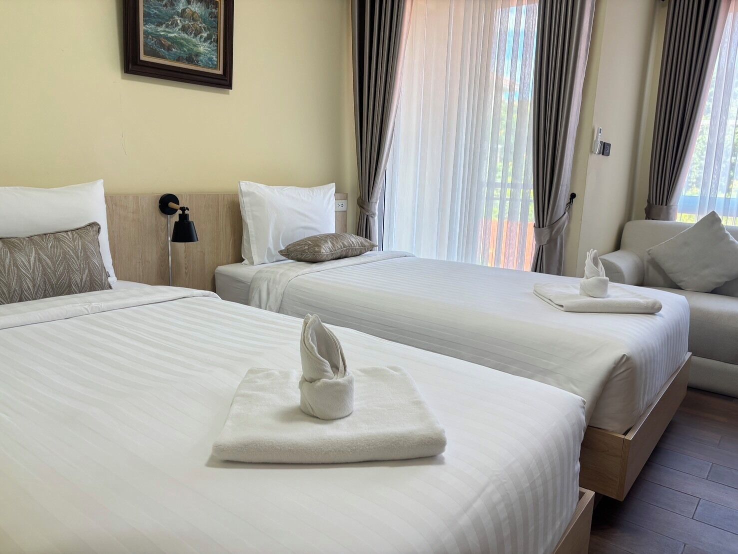A hotel room with two beds, a sofa, a painting on the wall, and a window with curtains.