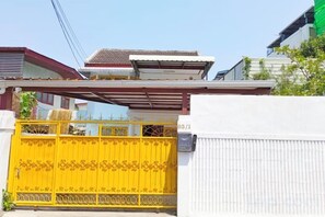 Una entrada protegida por un portón metálico, un muro blanco y una estructura de techo rojo.
