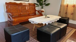 A living room with a wooden sofa, a small table with a lace tablecloth, and two black leather ottomans. - Ayana Homestay (Labuan)