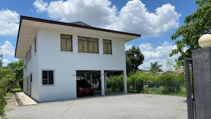 A two-story house with a garage, a car parked inside, and a paved driveway. - Ayana Homestay (Labuan)