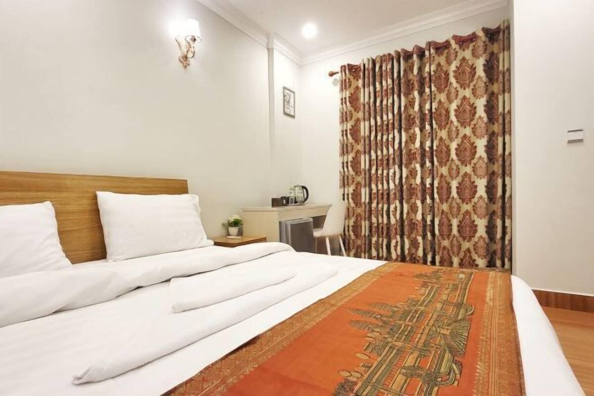 A neatly made bed with white linens, a wooden headboard, and an orange patterned bedspread.